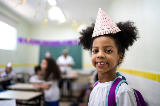 verticale d’une fille mignonne utilisant un chapeau de partie dans une partie d’anniversaire à l’école - fête de lécole photos et images de collection