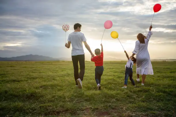 Photo of Asian family holding balloon and walking on the Meadow at sunset with happy emotion. Family Holiday and Travel concept.