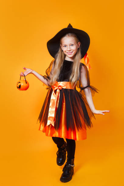 Cute happy little girl dressed up as witch with bucket of candy on orange background Cute happy little girl dressed up as witch with bucket of candy on orange studio background halloween pumpkin human face candlelight stock pictures, royalty-free photos & images