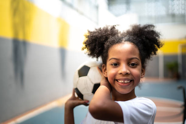 身体活動の授業中にサッカーボールを持つ幸せな女の子の肖像画 - ball horizontal outdoors childhood ストックフォトと画像