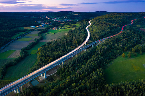 Aerial view of highway splitting aound forest hill on autumn evening, long exposure