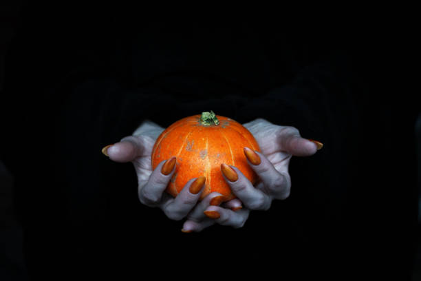 istock Happy Halloween theme. Small pumpkin in witches pale knotty hands with sharp long nails, low key, selected focus. 1280919948