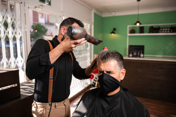 barbiere pettina e soffia i capelli di un altro uomo in un barbiere durante la pandemia di coronavirus. - backcombed foto e immagini stock