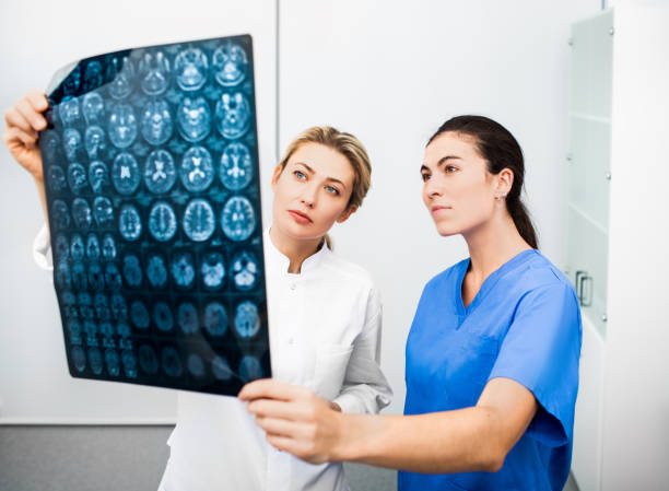 experienced woman neurologist and radiologist are looking at an mri scan of a patient's head. diagnostics and treatment of brain diseases, headaches, tumors and brain cancer - x ray image radiologist examining using voice imagens e fotografias de stock