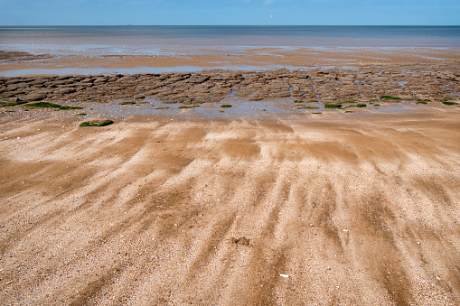 Mixed textures on the beach at Hunstanton in Norfolk, Eastern England, overlooking The Wash: streaky sand, rocks, pools of water, sea and sky.