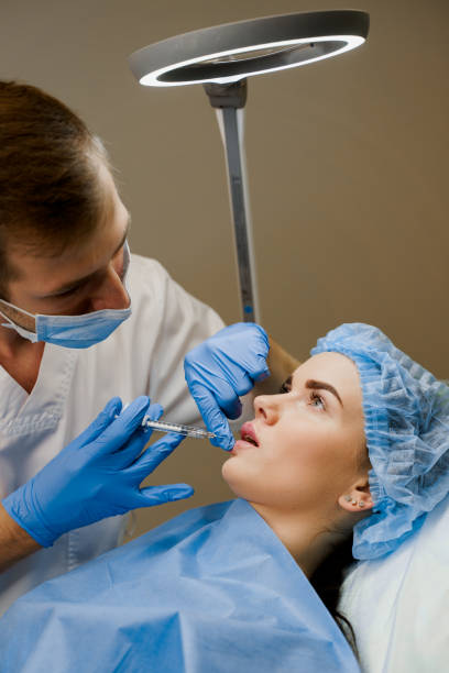 istock Lips augmentation injections for attractive girl. Plastic surgeon does injection in lip in medical clinic. Cosmetic rejuvenating facial treatment. Empty space for advert 1280931531