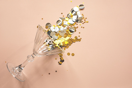 Wine glass with gold sparkles or confetti on a pink background. Celebration concept.