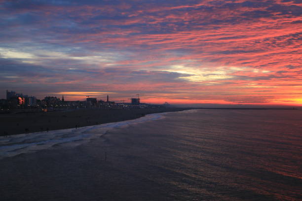 A beach with a view over the city during a sunset showing a bright red or orange colored cloudscape