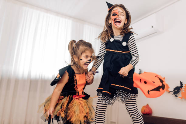 zwei aufgeregte mädchen in halloween-kostümen auf dem bett springen - child jumping vegetable food stock-fotos und bilder