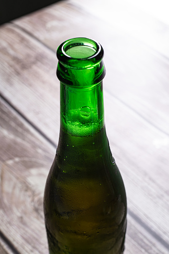 Full green blond beer bottle opened on a wooden surface close up still
