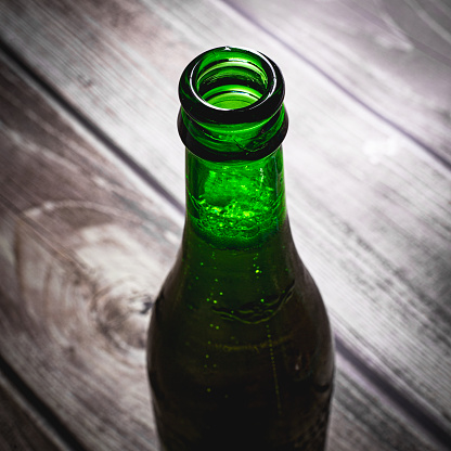 Full green blond beer bottle opened on a wooden surface close up still