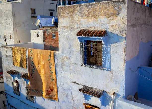 Photo of Carpets draped over wall of the residential house. Chefchaouen town, Morocco. Medina of the Blue city. Charm of the oriental life. Drying in the sun.