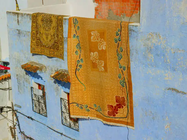 Photo of Old carpets dried in the sun on the wall of the residential house. Medina of the Blue city of Chefchaouen town, Morocco. Real of the oriental life.