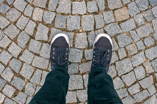 Feet in black trousers and sneakers stand on the cobblestones