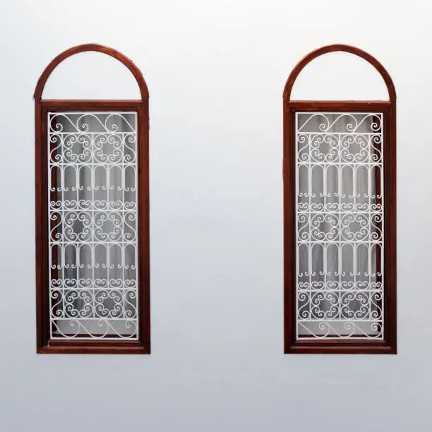 Photo of Two narrow windows decorated with decorative lattice on a white plastered wall. Moroccan authentic interior traditional for medina quarter at Marrakesh