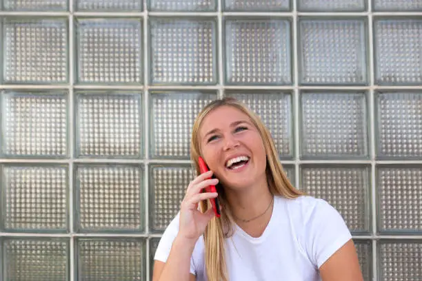Blond woman holding a red mobile phone on her right hand while talking to someone