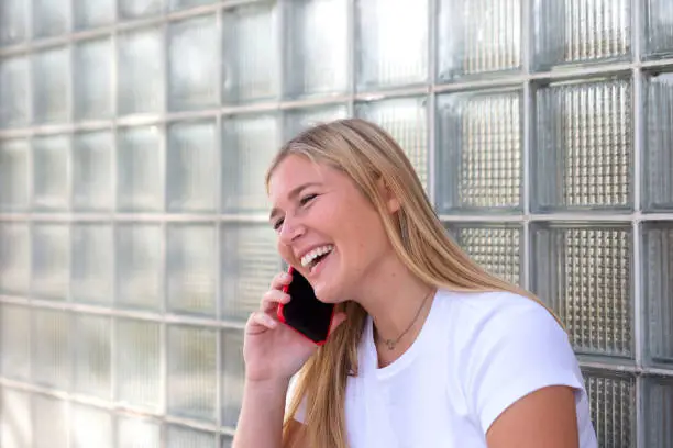 Blond woman holding a red mobile phone on her right hand while talking to someone
