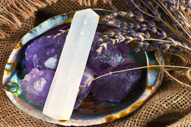 An image of an abalone shell filled with amethyst crystals and white selenite on old burlap textile.