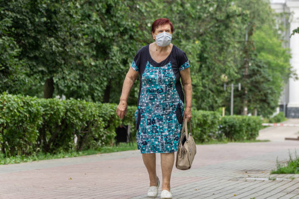 Lonely elderly woman wearing protective medical mask walking down the street in the city. stock photo