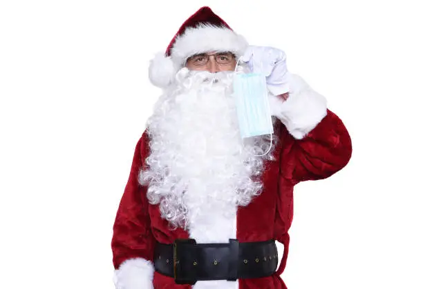 Senior man wearing a traditional Sant Claus costume holding a surgical mask reminding everyone to Mask Up during the  Covid-19 pandemic.