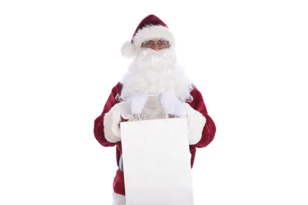 Senior man wearing a traditional Santa Claus costume holding a large gift bag in both hands.  Isolated on white.