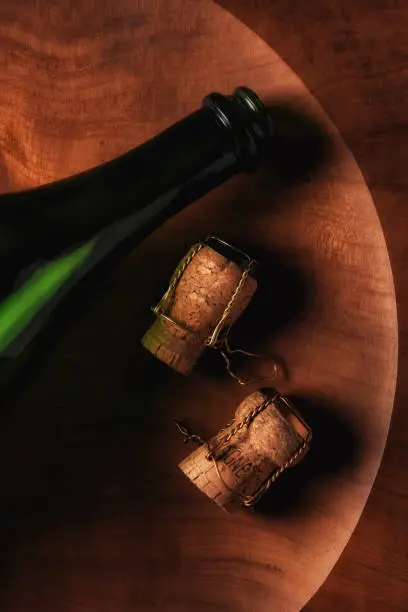 Flat lay still life of a champagne bottle and corks onb a round wooden platter.