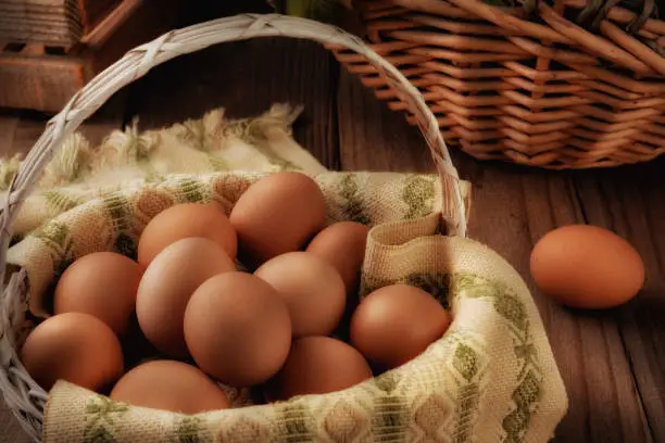 Stil llife with a basket full of brown eggs in a rustic farmhouse like setting, with warm side light.
