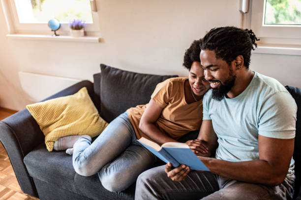 istock Husband and wife reading a book together on sofa. 1280985120