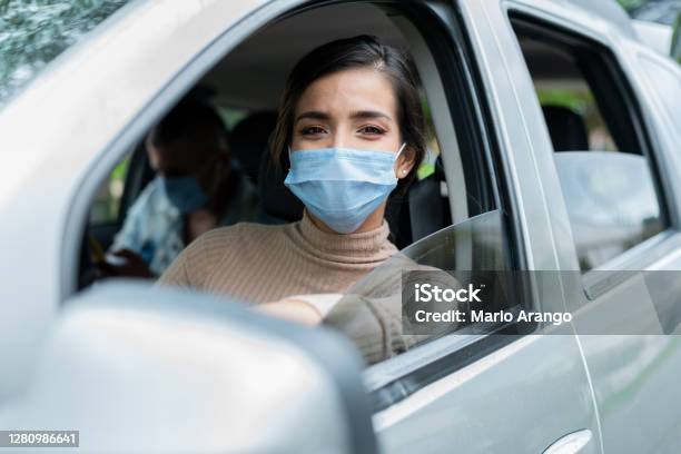 Beautiful Woman Looks At The Camera In A Portrait And Checks Her Cell Phone Waiting For A Service To Offer While Wearing Her Mask Stock Photo - Download Image Now