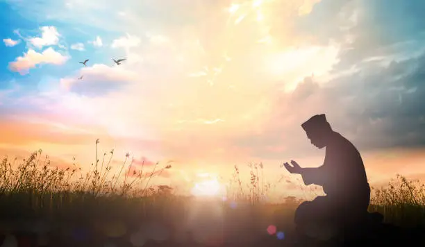 Muslim dua to Allah over meadow sunset background