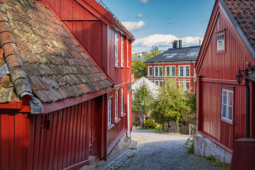 Beautiful red wooden houses in old town village in Damstredet Cobblestone Street in Oslo under blue summer sky. One of the oldest streets in the historic center of Oslo, Capital of Norway. Damstredet, Oslo, Norway, Scandinavia