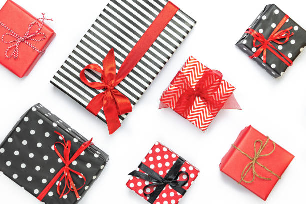 istock Gift boxes wrapped in black and white striped, dotted and red paper with wrapping materials over a white background. Various designs wrapped presents preparation. Copy space. 1280994267