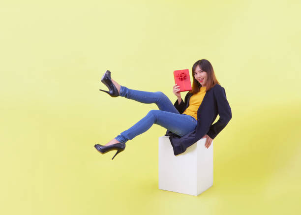 istock Attractive asian girl holding gift sitting on white cube 1280994364