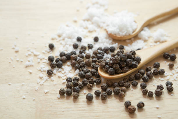 Black pepper and salt in wooden spoon on the kitchen table and copy space
