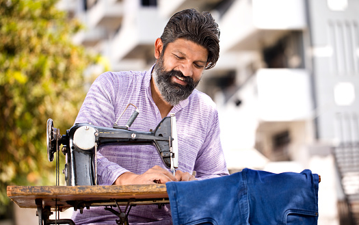 Happy Indian man sewing clothes with sewing machine
