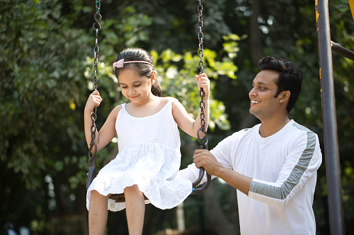 Happy father with cute daughter on amusement park swing