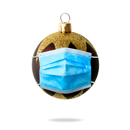 Purple Christmas ball wearing blue protective medical mask in mid air, against white background.