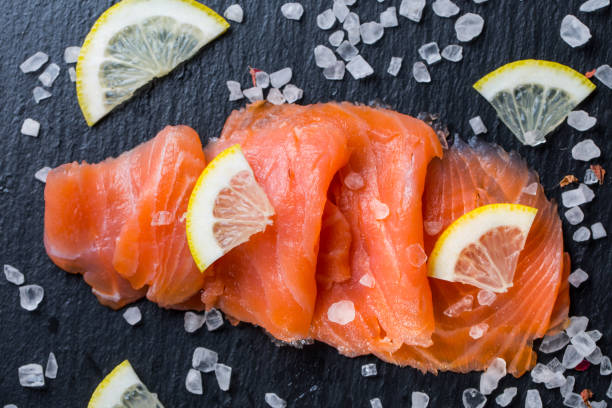 salmone affumicato con limone e sale marino su sfondo nero. - affumicato foto e immagini stock