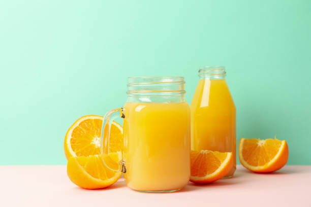 istock Glass jars with orange juice against mint background 1281009468