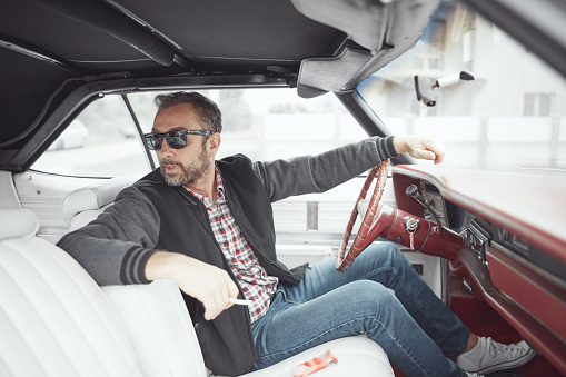Man in retro clothes holding cigarette and driving vintage American car.