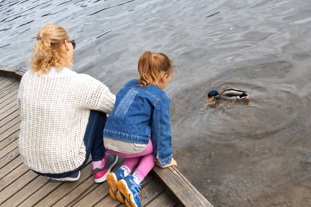 istock Mother and daughter feeding duck on a lake. 1281009608