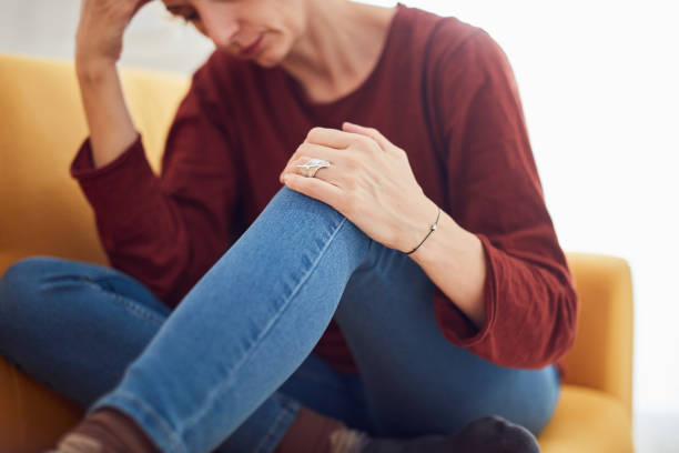 istock Woman with knee and headache problem sitting on a couch at home. 1281010468