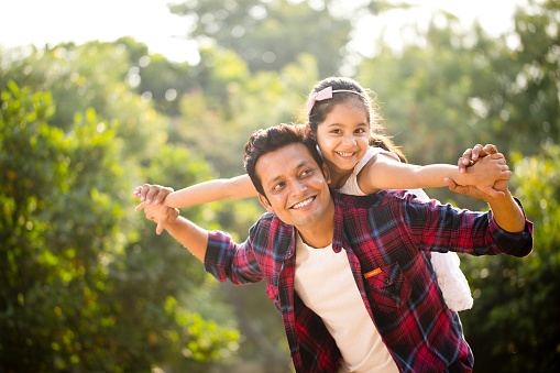 Happy father and daughter enjoying a piggyback ride at park