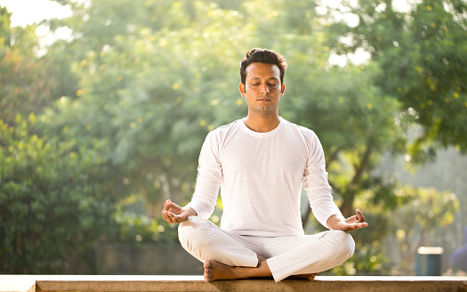 Man in white sportswear meditating outdoors at park