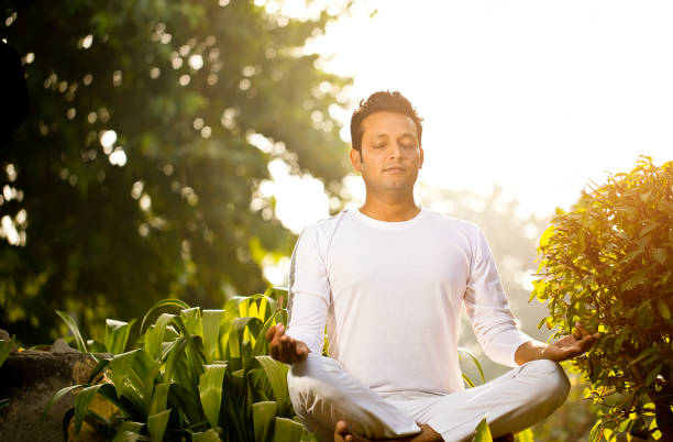 Full length of a healthy young man meditating in lotus position on exercise mat. Vertical shot. Isolated on white.