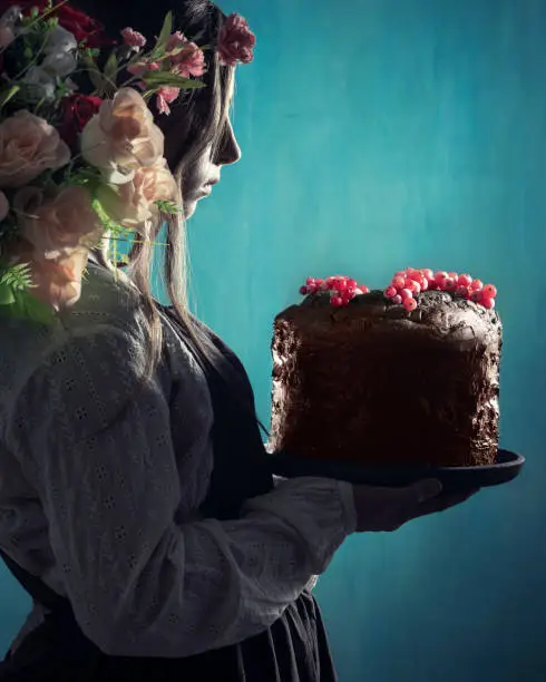 Vintage romantic girl holding chocolate cake with red curran berries and flowers in hair