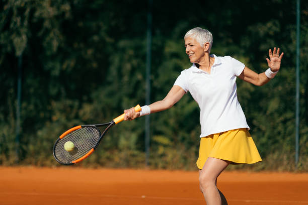 smiling elderly woman playing tennis as a recreational activity - tennis women one person vitality imagens e fotografias de stock