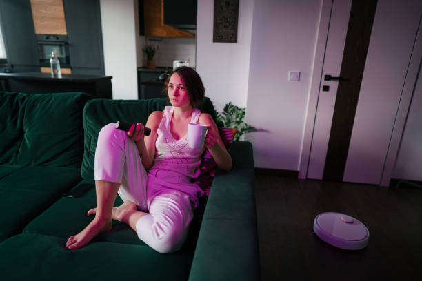 istock Woman using robot vacuum while sitting on the sofa and watching TV 1281031417