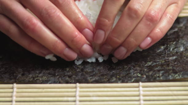 istock Spreading Cooked Sushi Rice On A Seaweed Wrap - Sushi Making - close up, slow motion.Sushi Chef Spreading Japanese Sushi Rice On Nori Sheet For A Delicious Sushi Rolls high angle shot 1281031971