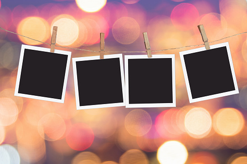 Four blank instant photo frames hanging on a rope, on holiday lights bokeh background